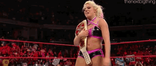a woman is holding a wrestling championship belt in a wrestling ring .