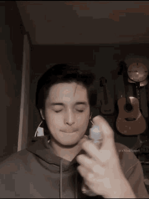 a young man is spraying something on his face in front of a wall of guitars .