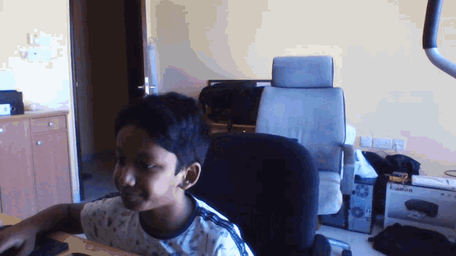 a young boy sits at a desk in front of a canon printer
