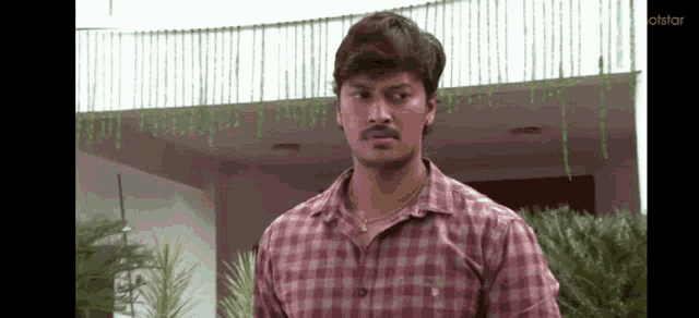 a man in a plaid shirt is standing in front of a building with a necklace around his neck .