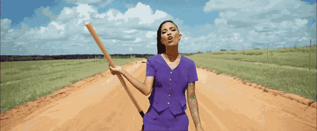 a woman in a purple dress is holding a wooden bat