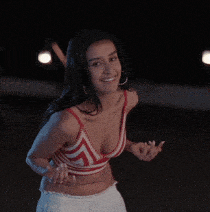 a woman in a red and white striped top and white skirt is dancing in the dark .