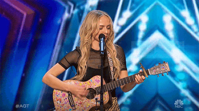 a woman is singing into a microphone while playing a guitar on nbc