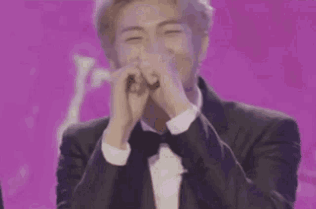 a man in a tuxedo is making a heart with his hands .
