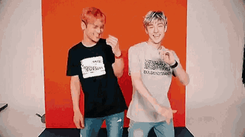 two young men are standing next to each other in front of an orange wall .