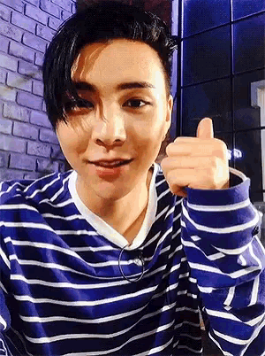 a young man wearing a blue and white striped shirt is giving a thumbs up sign .