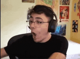 a man wearing headphones and glasses is making a funny face while sitting at a desk .