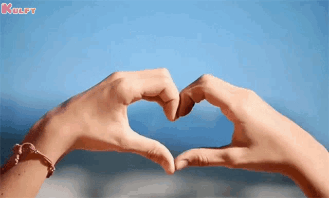 a person is making a heart shape with their hands on a beach .