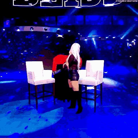 a woman is standing in front of two chairs in a dark room with a sign that says ethenextbigthing