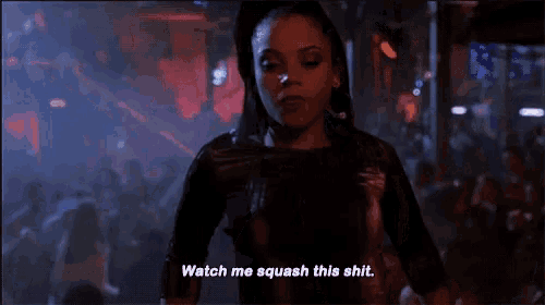 a woman is standing in front of a crowd in a dark room and saying `` watch me squash this shit '' .