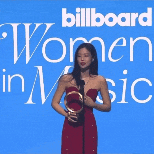 a woman in a red dress is holding an award in front of a sign that says billboard women in music