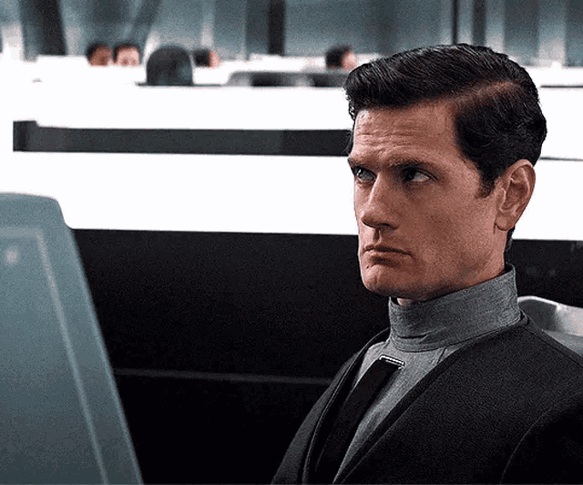 a man in a suit and tie is sitting in front of a computer monitor