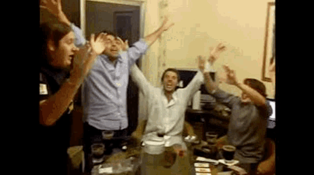 a group of people are standing around a table with their arms in the air .