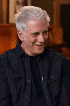 a man with gray hair is wearing a black shirt and smiling .