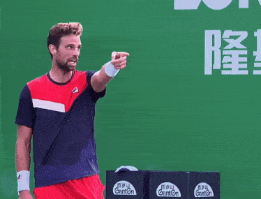 a man is holding a tennis racquet in front of a green wall with chinese writing on it