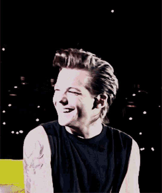 a man with a tattoo on his arm is smiling in a black tank top