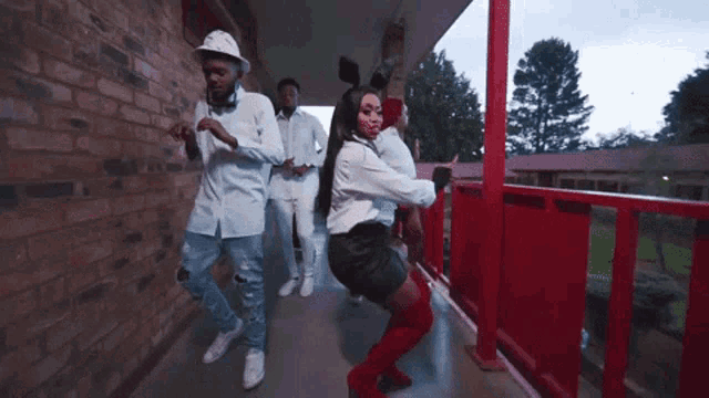 a group of people are dancing on a balcony with a red railing .