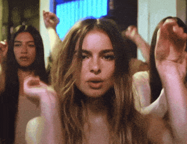 a woman with long hair stands in front of a group of women with their hands in the air