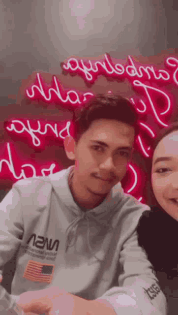 a man and a woman are sitting at a table in front of a neon sign .