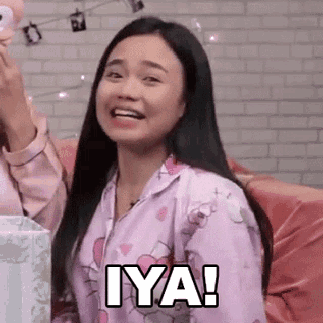 a woman in a pink pajama top is sitting on a couch and smiling .