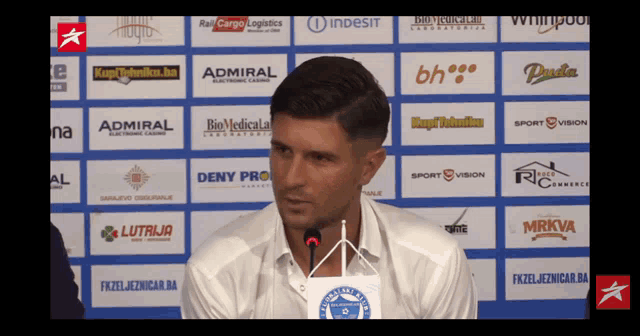 a man in a white shirt stands in front of a wall of logos including admiral and indesit