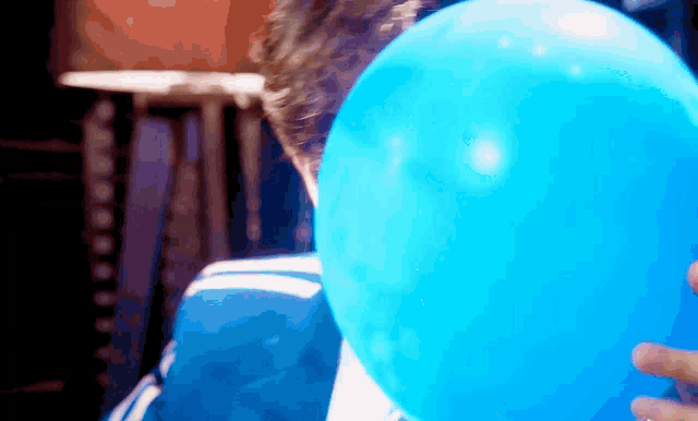 a person blowing up a blue balloon with their face