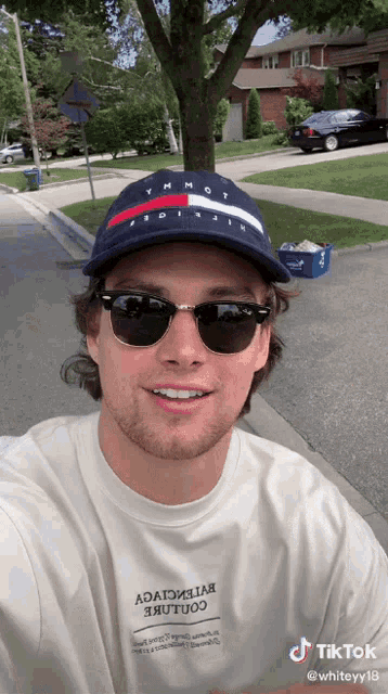 a man wearing a tommy hilfiger hat and sunglasses is taking a selfie