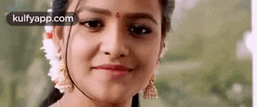 a close up of a woman 's face with a flower in her hair and earrings smiling .