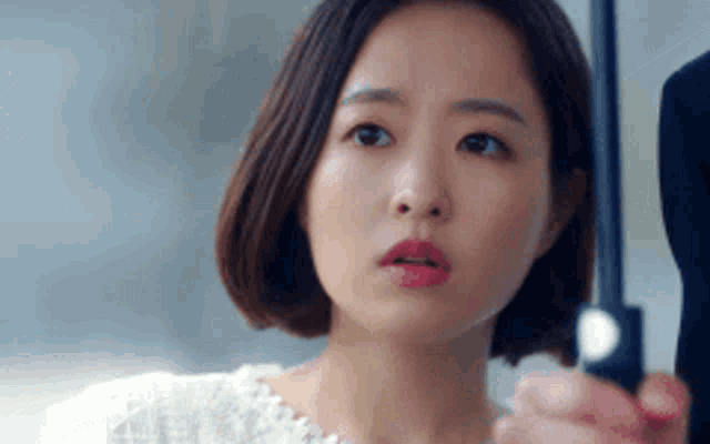 a woman with short hair is holding an umbrella and looking at the camera .