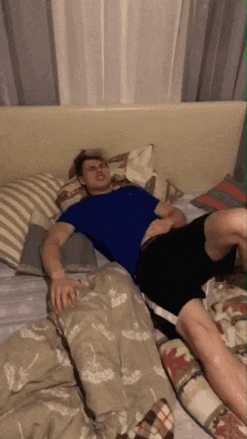 a man in a blue shirt is laying on a bed with pillows