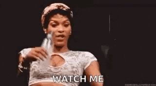 a woman in a crop top is holding a bottle of water and says `` watch me '' .