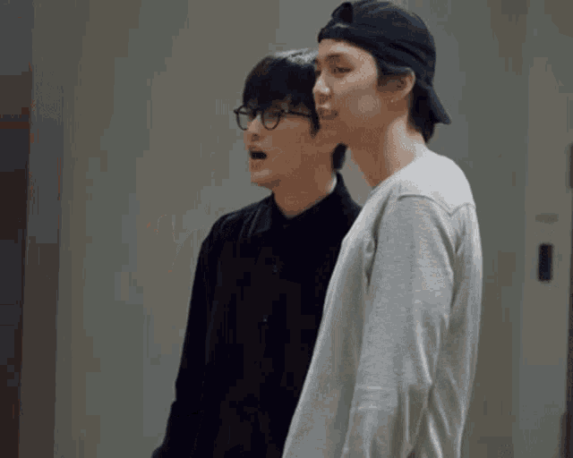 two men are standing next to each other and one is wearing a baseball cap