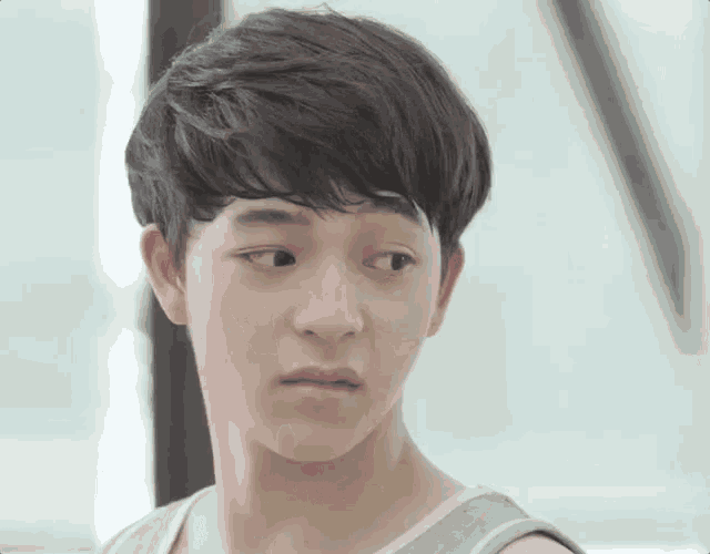a close up of a young man 's face with a gray tank top on