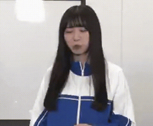 a woman with long black hair is wearing a blue and white jacket and making a funny face .