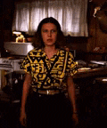 a woman wearing a yellow and black shirt and suspenders is standing in a kitchen .