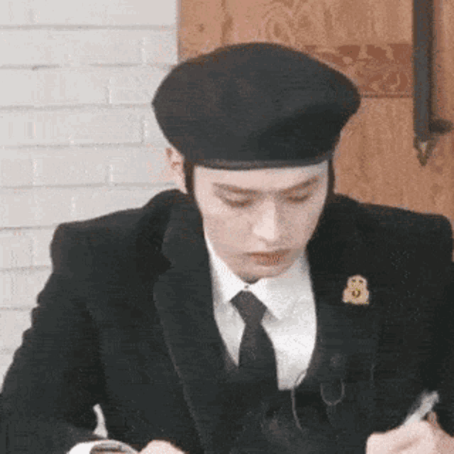 a man in a suit and tie is wearing a black beret and looking at his phone .