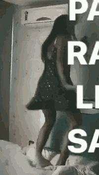 a woman in a dress is dancing on a bed in front of an air conditioner in a room .