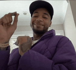 a man wearing a purple jacket and a black hat holds something in his hand