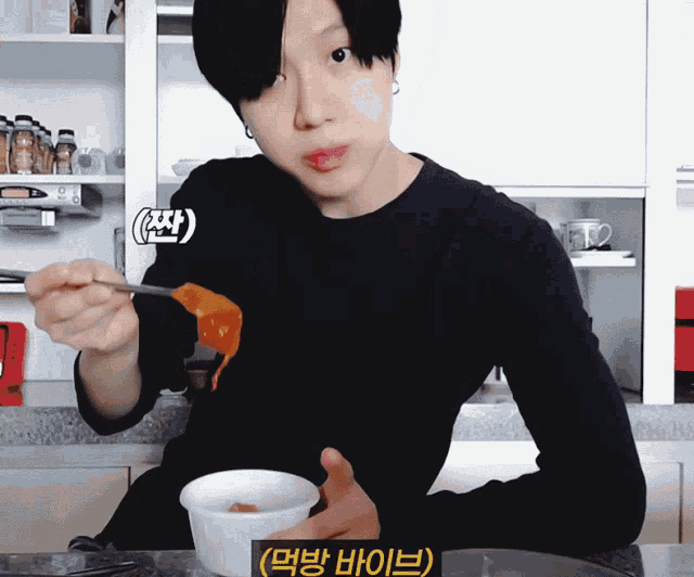 a man in a black shirt is holding a spoon and eating food