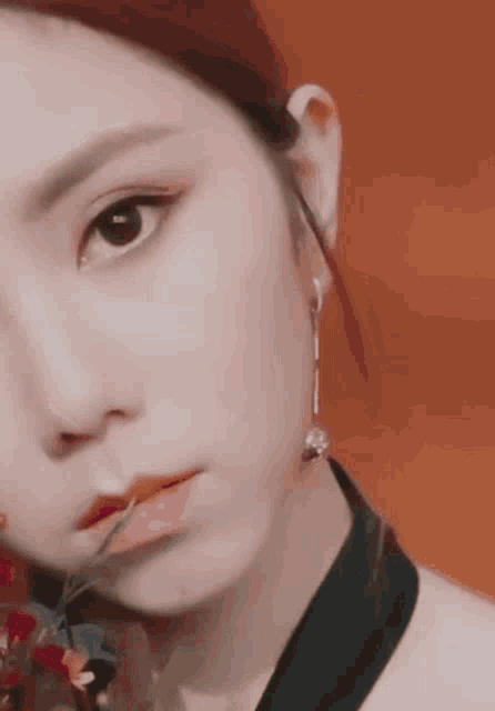 a close up of a woman 's face with a flower in her mouth and earrings .