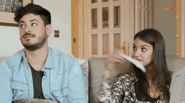 a man and a woman are sitting on a couch and the man is looking up at something