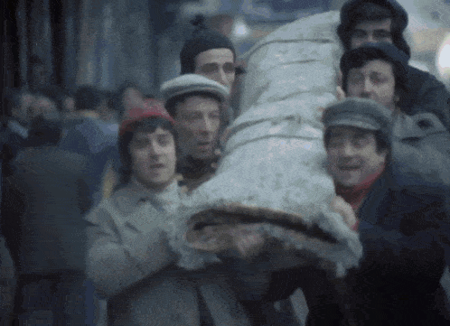 a group of men are carrying a large bag on their backs