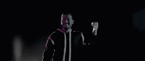 a man in a black jacket is holding his fist up in the air in the dark .