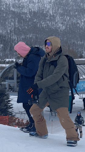 a man wearing a hooded jacket stands next to a woman wearing a pink beanie