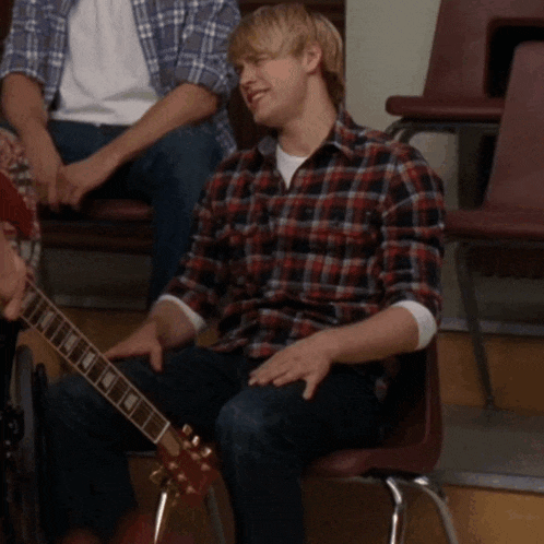 a man in a plaid shirt is sitting in a chair holding a guitar
