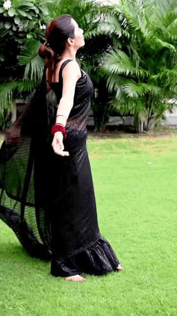 a woman in a black dress stands on a lush green field