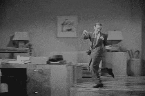 a black and white photo of a man in a suit and tie dancing in an office .