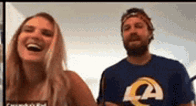 a man and a woman are laughing together on a video call . the man is wearing a la rams shirt .