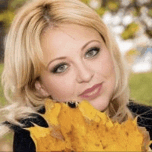 a woman with blonde hair is holding a yellow leaf in her mouth .