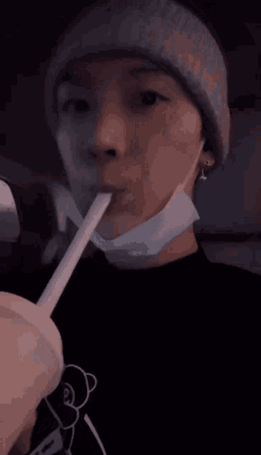 a person wearing a beanie is drinking through a straw from a cup